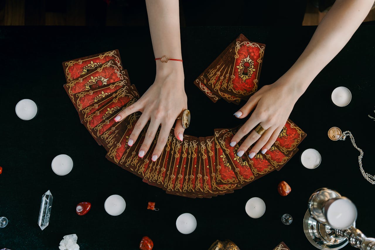 Hands arranging tarot cards on a table surrounded by candles and crystals, creating a mystical ambiance.